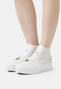  Hoge sneakers van wit suède met witte veters, een textuur bovenkant en een dikke witte platformzool. Bevat een zijlogo accent.