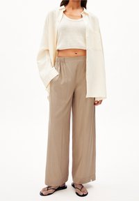 Béžové široké kalhoty s elastickým pasem, spárované se zkráceným krémovým pleteným topem a oversized krémovou košilí na knoflíky. Černé žabky.