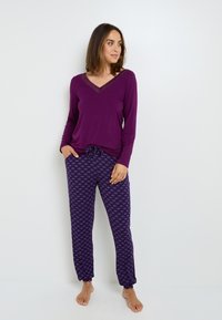 Haut à manches longues violet avec un décolleté en V, associé à un pantalon violet à motifs présentant de petits motifs. Tissu doux, coupe décontractée.