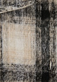 Vlněná látka v kostkovaném vzoru s béžovými, černými a šedými odstíny. Texturovaný povrch s měkkými, chlupatými vlákny a viditelným prošíváním.