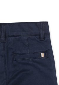 Pantaloni in misto cotone blu navy con una texture liscia, dotati di una tasca posteriore con un dettaglio a strisce orizzontali in nero, bianco e beige.