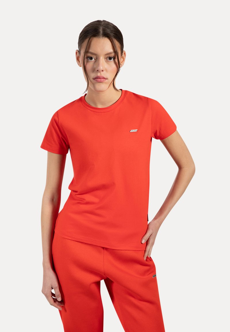 Camiseta roja de manga corta, hecha de una tela suave, con un escote redondo y un pequeño parche de logo en el lado izquierdo. Diseño ajustado.