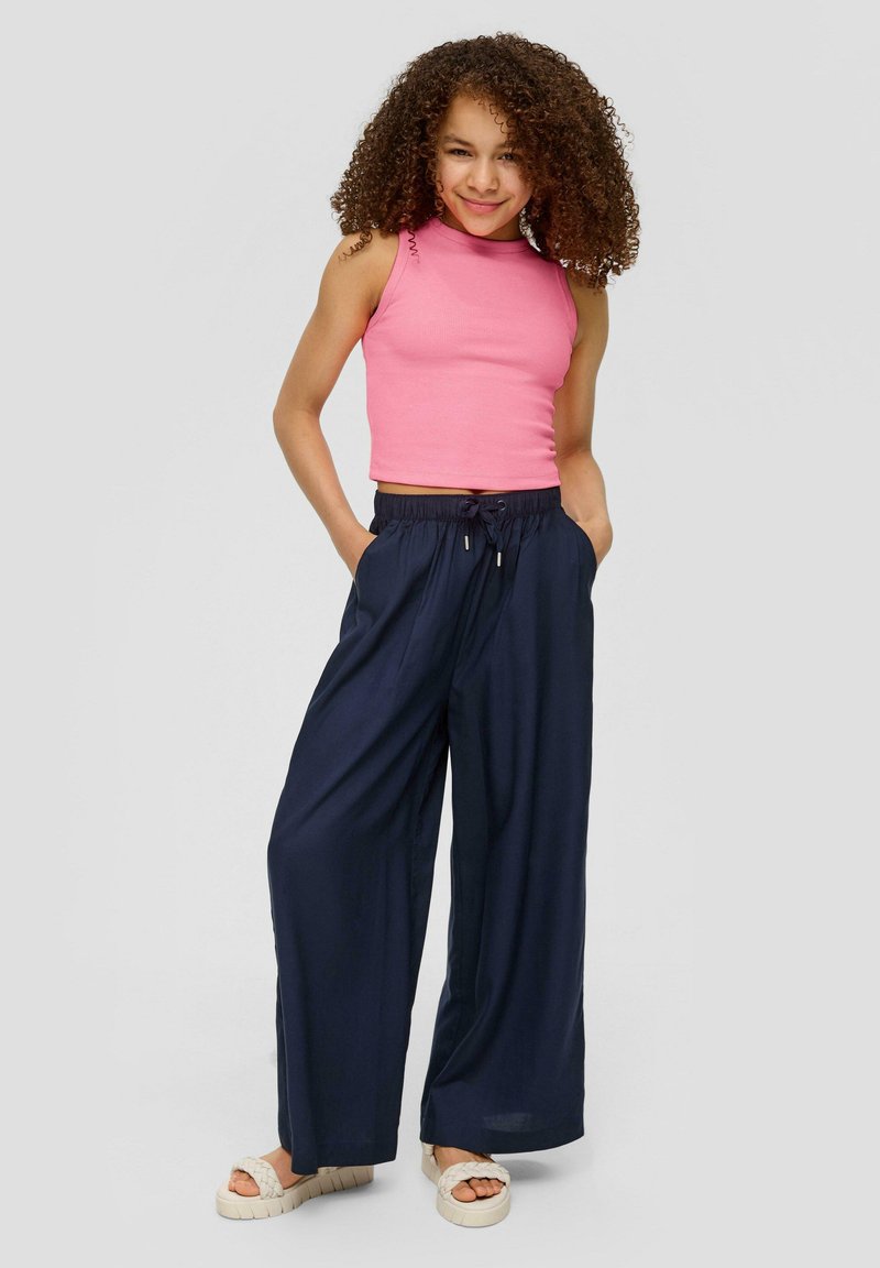 Roze mouwloze top gecombineerd met navy wijde broek met elastische tailleband en trekkoord. Model draagt lichtgekleurde platform sandalen.