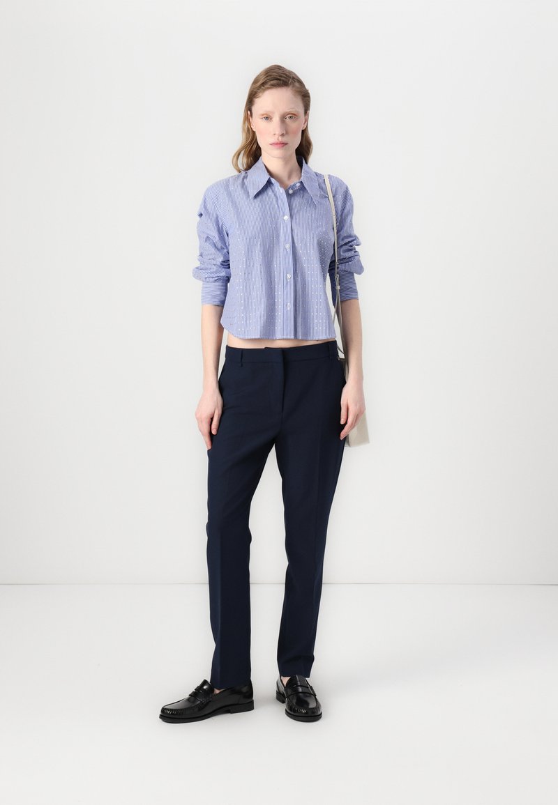 Camicia blu a righe con colletto, abbinata a pantaloni blu scuro a vita alta e mocassini neri. Design minimalista, texture lisce.