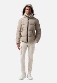 Beige pufferjack met capuchon, voorzien van een rits aan de voorkant, zijzakken en een geweven ontwerp. Gecombineerd met crèmekleurige cargobroek en witte sneakers.
