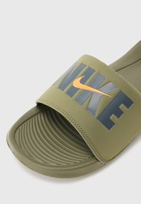 Chancla verde con una plantilla texturizada. La parte superior presenta un logo "NIKE" en gris oscuro con un acento en forma de swoosh naranja.