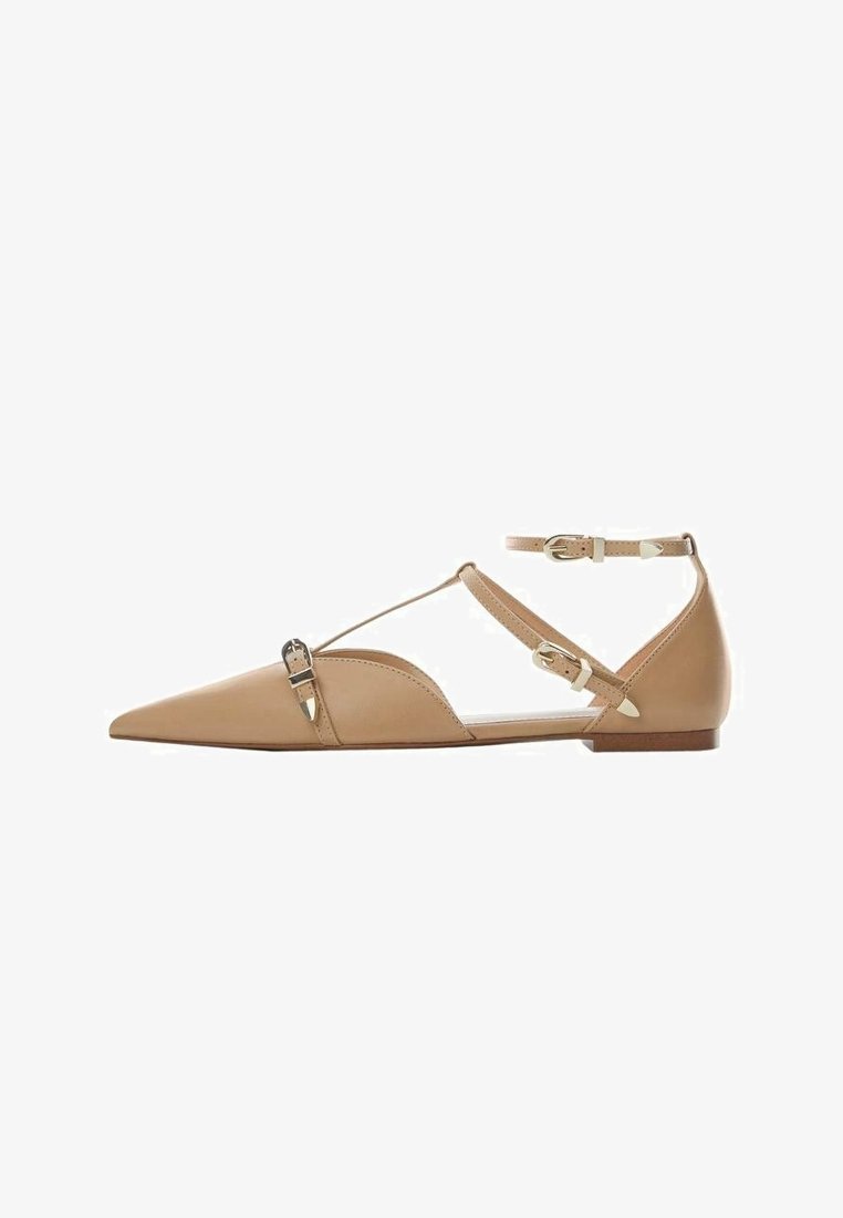 Chaussures plates en cuir beige avec un bout pointu, dotées de brides de cheville et d'accents de boucle en or. Texture lisse avec des éléments de design découpés.