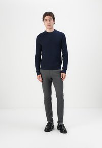 Marineblauer gerippter Pullover, Rundhalsausschnitt, getragen mit grauen Slim-Fit-Hosen und schwarzen Schuhen. Einfaches Design mit einem strukturierten Muster.