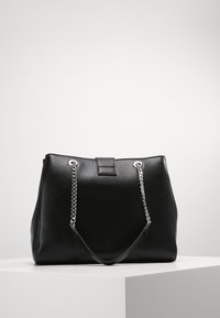 Sac à main noir en matériau texturé, avec des poignées en chaîne argentée et un fermoir rectangulaire. Design structuré avec une large ouverture.