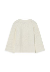 Ljusbeige stickad tröja med ribbad nederkant, vida ärmar och ett strukturerat mönster över hela plagget. Finns med öppen rygg.