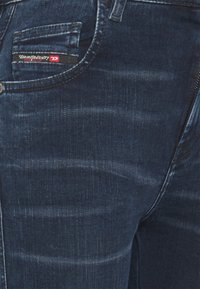 Mörkblå denimjeans med subtil blekning, en framficka med en röd och svart etikett, och en jämn textur.