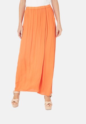 Larga y fluida falda maxi naranja con una cinturilla fruncida, hecha de tela ligera, combinada con zapatos de tacón alto color beige.