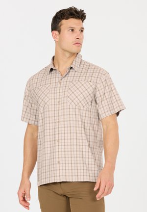 Mann trägt beige kurzärmeliges kariertes Hemd und braune Hose, blickt nach links vor einfachem Hintergrund.