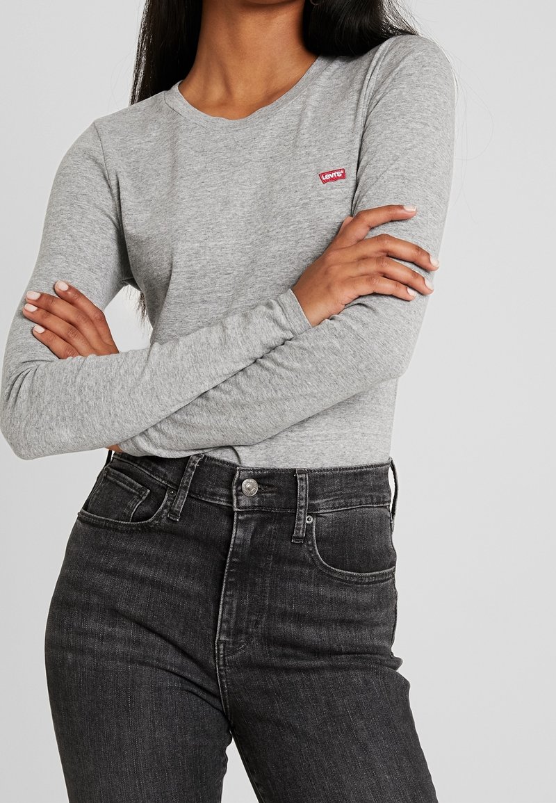 Graues langärmeliges T-Shirt aus weichem Stoff, mit einem roten Levi's Logo-Patch auf der Brust, kombiniert mit hochgeschnittenen schwarzen Jeans.