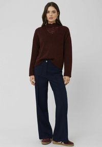 Pull en maille bourgogne avec des détails en dentelle, assorti à un pantalon large bleu marine avec poches avant et fermeture à bouton. Baskets marron aux pieds.