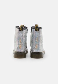 Srebrne botki na kostkę z teksturowanym, holograficznym wykończeniem. Z czarnymi zamkami błyskawicznymi i żółtymi uchwytami, osadzone na wytrzymałej brązowej podeszwie.