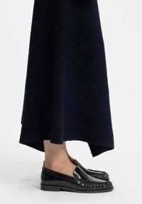 Μαύρα μοκασίνια με υφή και επίπεδο τακούνι, φορεμένα με ένα σκούρο μπλε πλεκτό φόρεμα με ελαφρώς φαρδύ τελείωμα.