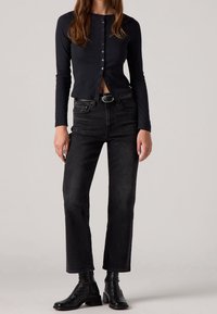 Haut noir à manches longues avec un devant boutonné, associé à un jean noir à coupe droite. Des bottines noires complètent la tenue. Design simple.