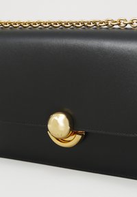 Borsa a pochette in pelle nera con tracolla in catena dorata, dotata di una chiusura metallica rotonda e una texture liscia. Design minimalista con cuciture a contrasto.