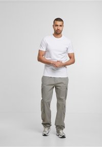 T-shirt en coton blanc associé à un pantalon cargo gris clair avec plusieurs poches, complété par des chaussures de sport argentées.