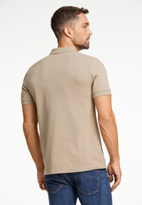 Beige pikétröja i texturerad tyg, med korta ärmar och ribbad krage, tillsammans med blå jeans.