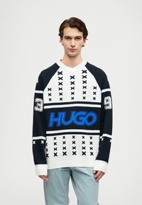Pleteni pulover v mornarsko modri in beli barvi z velikim modrim logotipom "HUGO", ki ima raglan rokave, geometrijske vzorce in rebraste manšete.