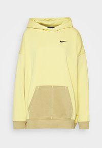 Felpa gialla con cappuccio, logo Nike nero, tasca a marsupio e pannello inferiore beige in contrasto. Tessuto morbido, vestibilità oversize.