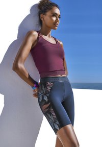 Maroon athletic tank top with thin straps paired with black cycling shorts featuring a floral side pattern. Smooth, stretchy material throughout.