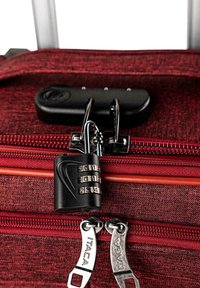 Maleta de tela texturizada roja con cerradura de combinación, cremalleras metálicas con grabado "ITACA" y un mecanismo de cierre negro.