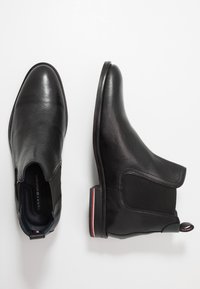 Botas chelsea de cuero negro con paneles elásticos en los laterales y punta redonda. Presentan un tacón bajo y un acento en rojo y blanco contrastante en la suela.