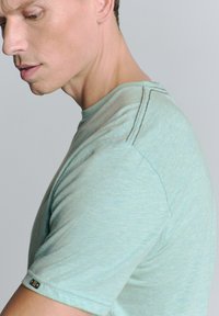 Lichtgroene t-shirt met korte mouwen en een subtiele gemêleerde textuur, voorzien van contrasterende stiksels en een klein logo op de mouw.