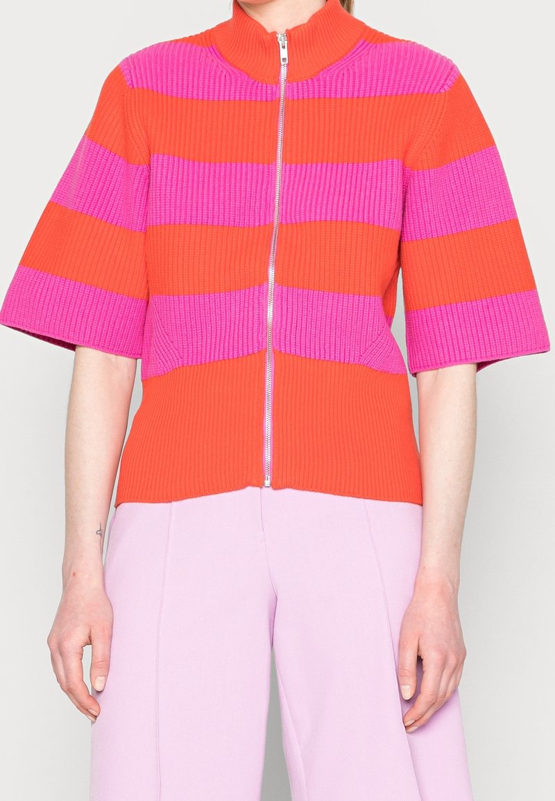 Stickad tröja i orange och rosa horisontella ränder, med hög krage och dragkedja, breda korta ärmar och ribbad textur.