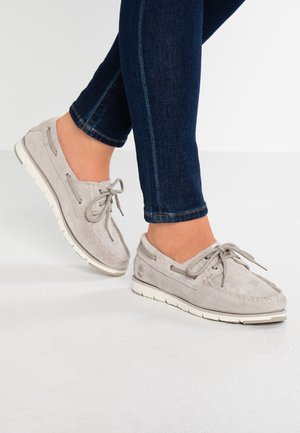 Gray suede boat shoes with white rubber soles, featuring laces and a stitched detail. Worn with dark blue skinny jeans.