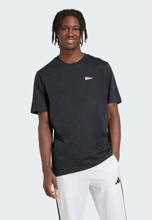 T-shirt nera a maniche corte in cotone, con un piccolo logo rosso sul petto a sinistra. Texture liscia, vestibilità casual.