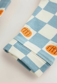 Tissu à carreaux bleu et blanc avec des illustrations de citrouilles orange, montrant un ourlet plié avec des coutures visibles.