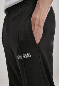 Sorte sweatpants lavet af blødt stof, med en sidelomme og hvid tekstdetalje på venstre ben. Elastisk talje for komfort.