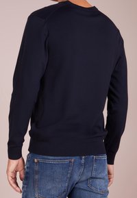 Maglione a girocollo blu navy realizzato in tessuto liscio, con maniche lunghe e polsini a costine. Indossato con jeans di denim, evidenziando un design aderente.
