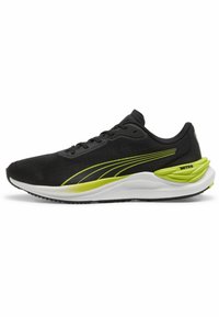 Zapatilla deportiva negra con parte superior texturizada, acentos verdes a los lados y una suela blanca acolchada. Cuenta con cordones y un diseño de punta redondeada.