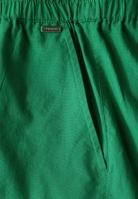 Zelené šortky vyrobené z lehké látky, s elastickým pasem, boční kapsou a malým metalickým logem.