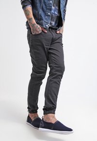 Tmavě šedé džíny s úzkým střihem a elastickými manžetami, doplněné námořnicky modrými slip-on botami s texturovanými detaily a bílými podrážkami.