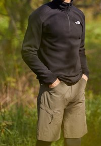 Pullover in pile nero con mezza cerniera e logo The North Face, abbinato a pantaloni cargo leggeri color oliva con tasche con zip.