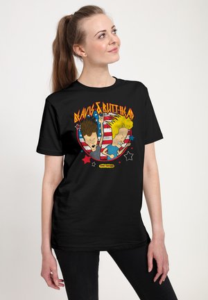 Ung kvinde med hestehale iført en sort "Beavis & Butt-Head" T-shirt med animerede figurer og et amerikansk flag i baggrunden.