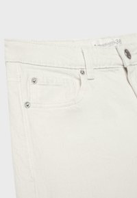 Gros plan d'un jean en denim blanc montrant la poche avant, les passants de ceinture, les rivets en métal et la fermeture par bouton argenté.