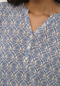 Blå blomstermønstret skjorte med V-hals, knaplukning og en struktureret beige baggrund. Bomuldsstof med en blød finish.