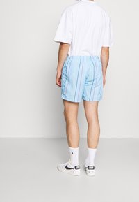 Ljusblå shorts med vertikala ränder i rosa, gult och lila. Elastiskt midjeband, ovanför knä-längd och en mjuk textur.