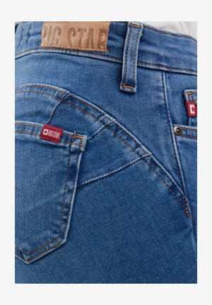 Blugi din denim albastru cu buzunare posterioare vizibile, cusături portocalii, etichete roșii cu marca Big Star și o etichetă de brand din piele maro pe talie.
