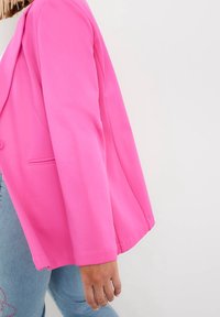 Różowy żakiet o usztywnionym kroju, z długimi rękawami, z jednym zapięciem na guzik oraz gładkim, elastycznym materiałem.
