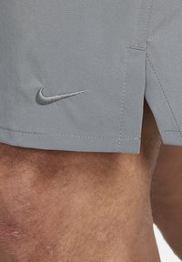 Short gris Nike avec une petite fente latérale porté au-dessus du genou poilu et de la partie inférieure de la cuisse d'un homme visible dans le cadre.