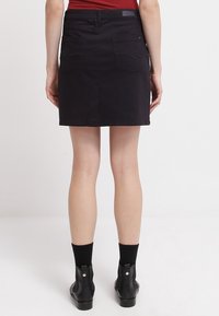 Schwarzer Jeansrock mit geradem Schnitt, zwei Gesäßtaschen und dezenten Steppnähten. Kombiniert mit schwarzen Stiefeletten.