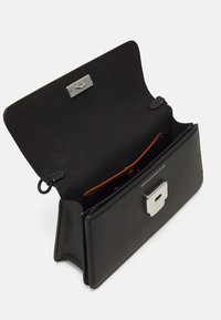 Bolso de mano de cuero negro con un cierre plateado, que cuenta con un amplio interior forrado de tela negra y un bolsillo de acento marrón.